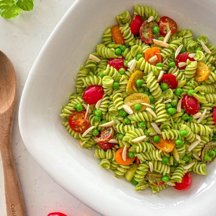 Large serving bowl with pesto pasta salad inside with cherry tomatoes and slivered almonds on top.
