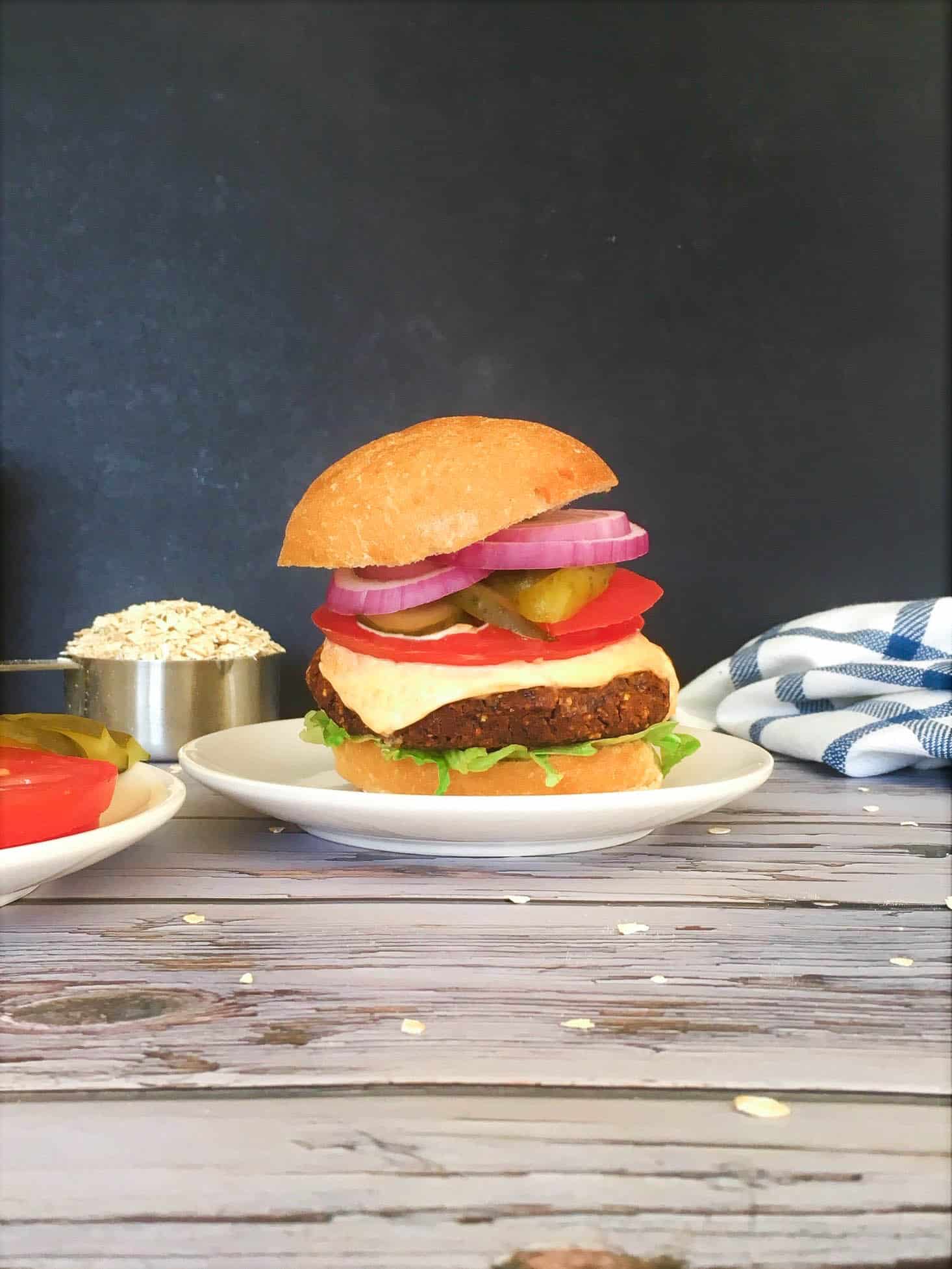 burger in bun on plate with tomato, pickles, onion, lettuce, mayo