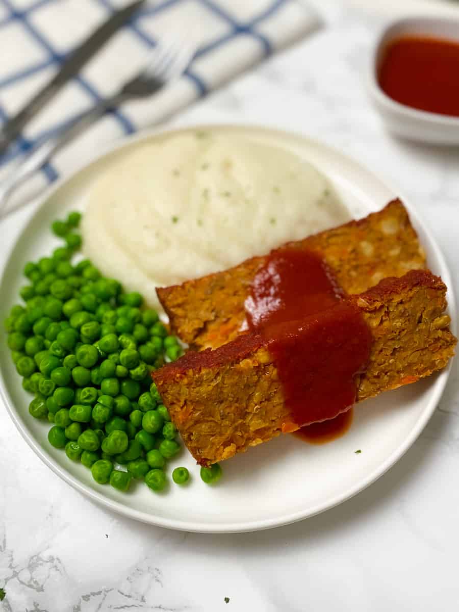 sliced vegan meatloaf with red sauce glazed on top and peas beside it.