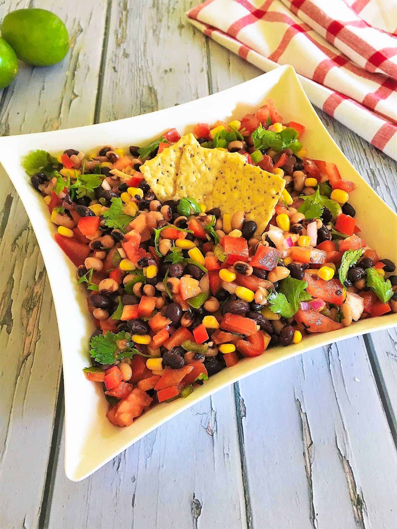 bean salad in white square bowl with crackers on top