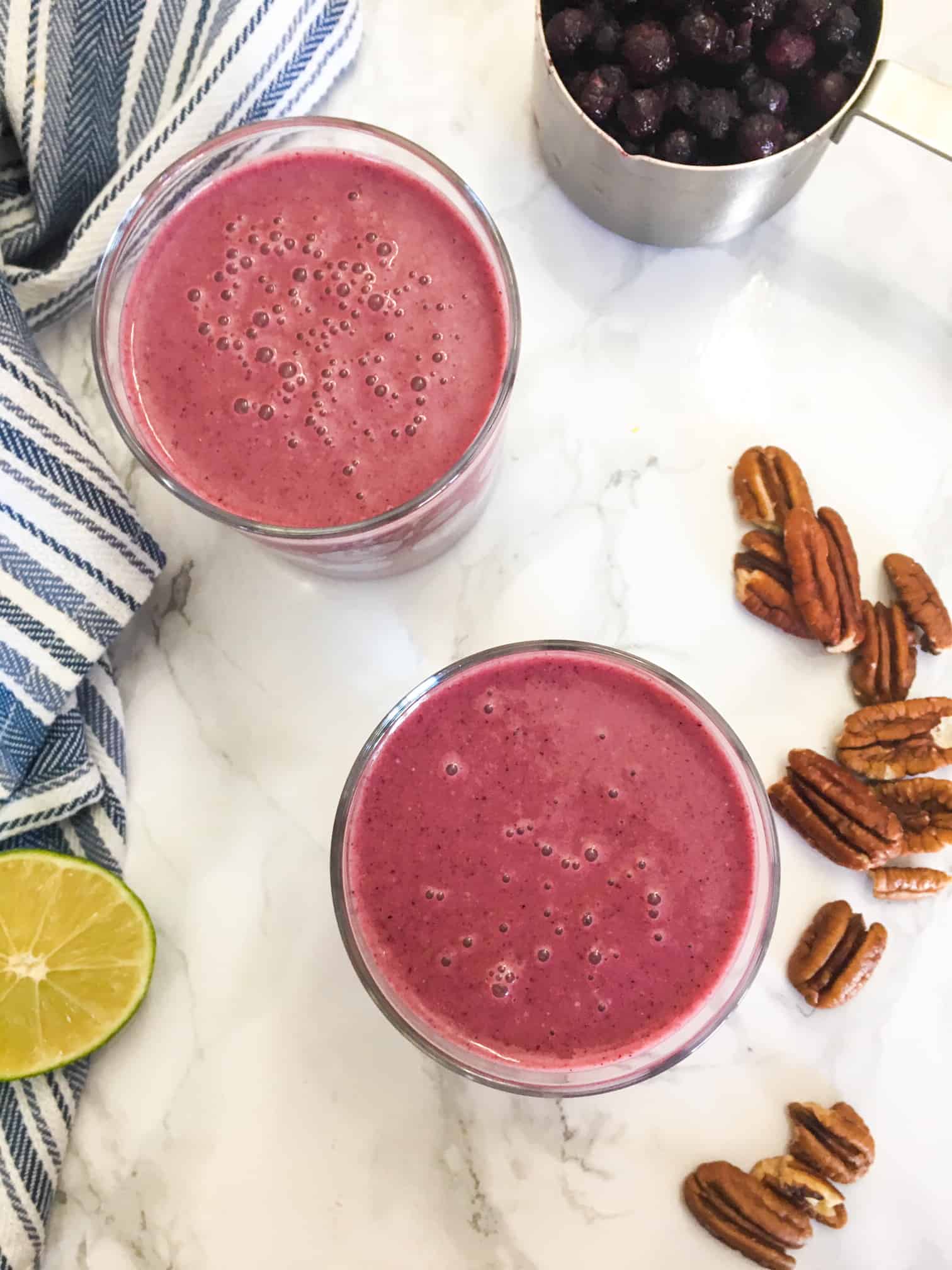 pink smoothie in two glasses with pecans scattered around the glass