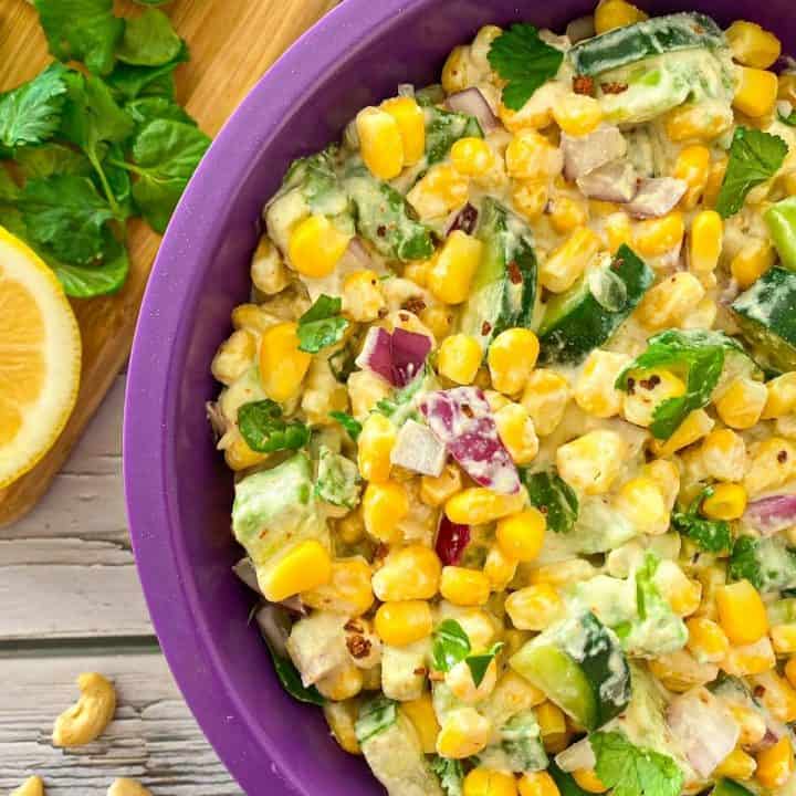 Bowl with corn salad and cutting board with cilantro, cucumber and lemon beside it.