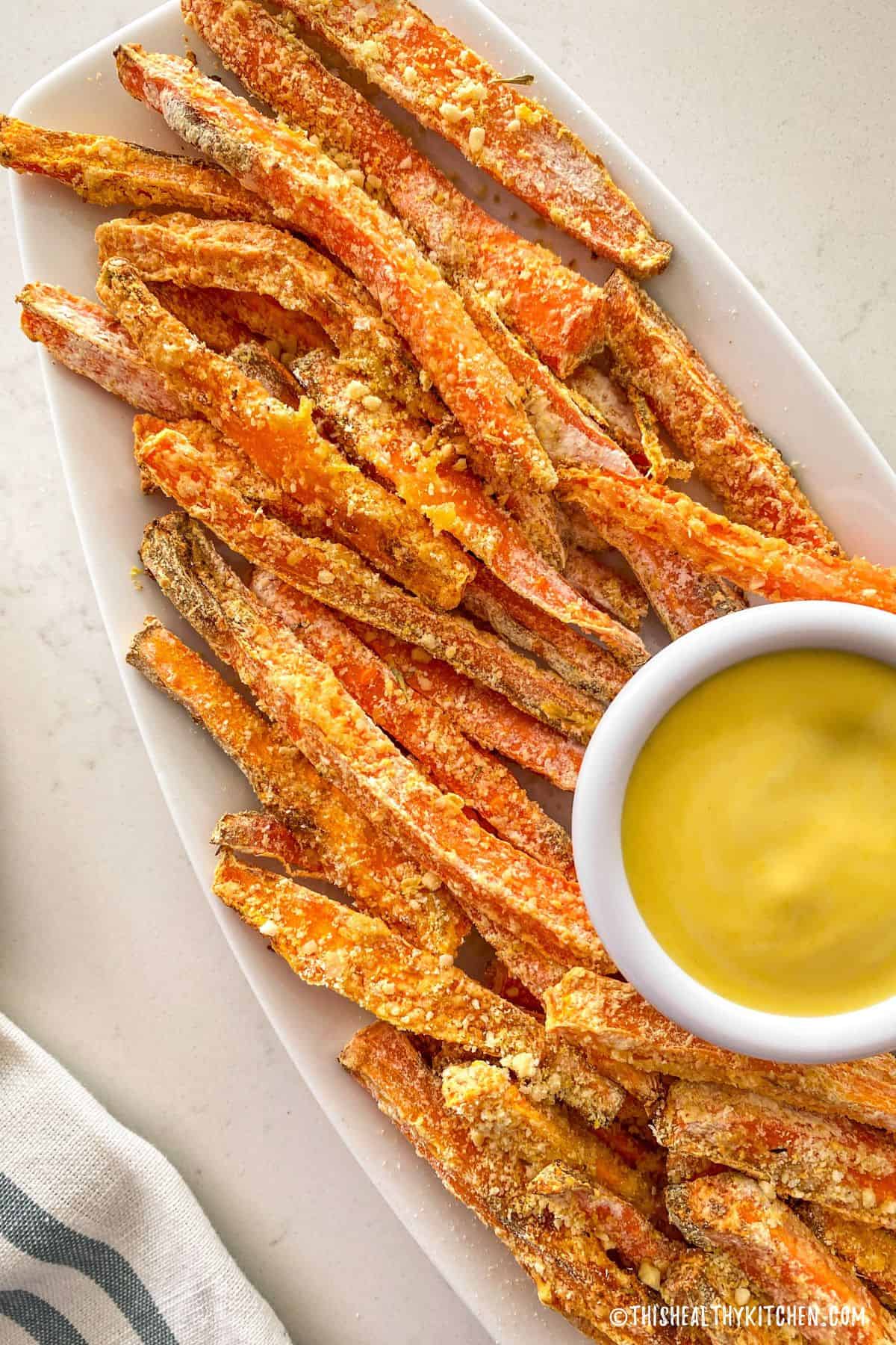 Carrot fries on white platter with yellow dipping sauce.