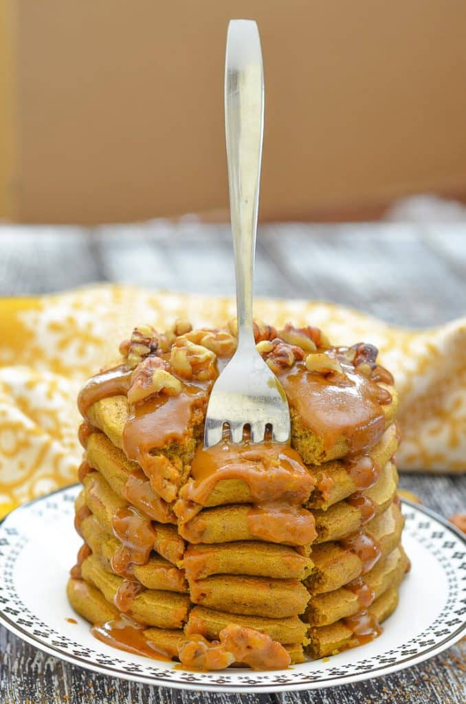 Stack of sweet potato pancakes with caramel dripping down the sides and fork standing up in the stack.