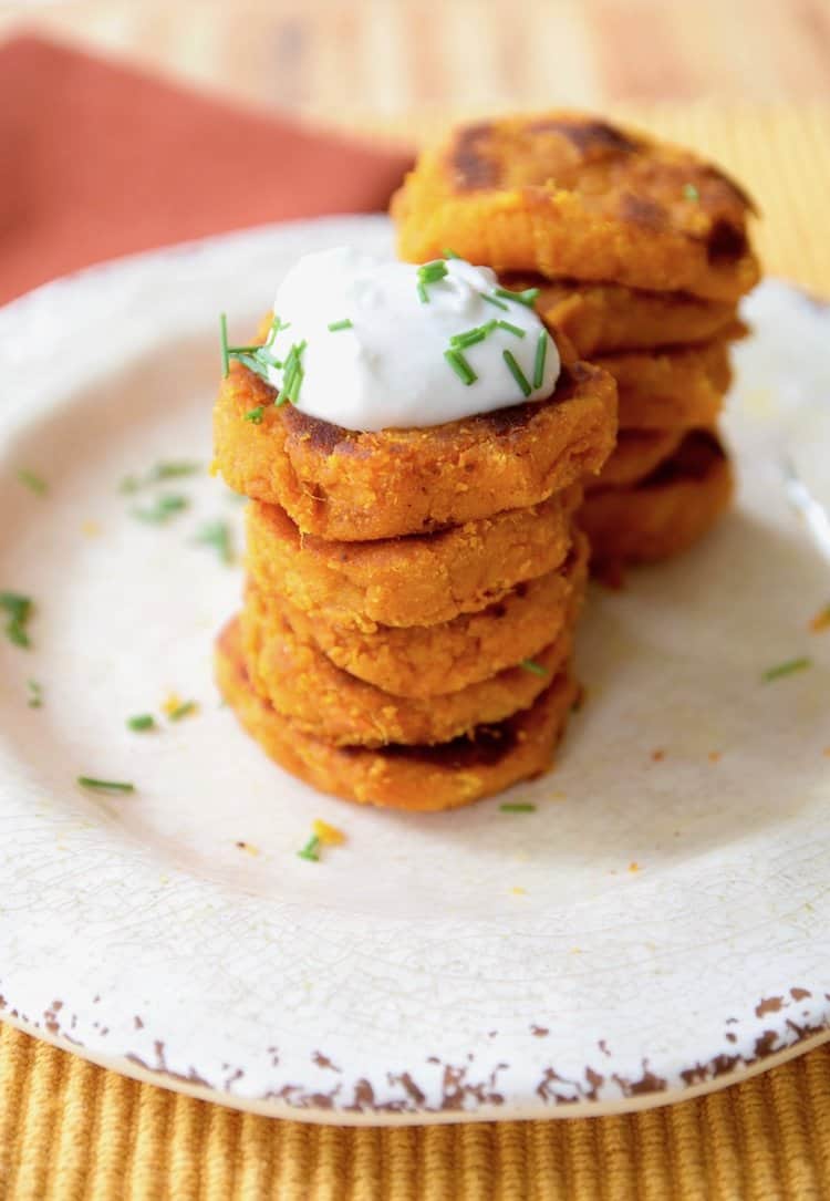 Stack of sweet potato fritters with white cream on top.