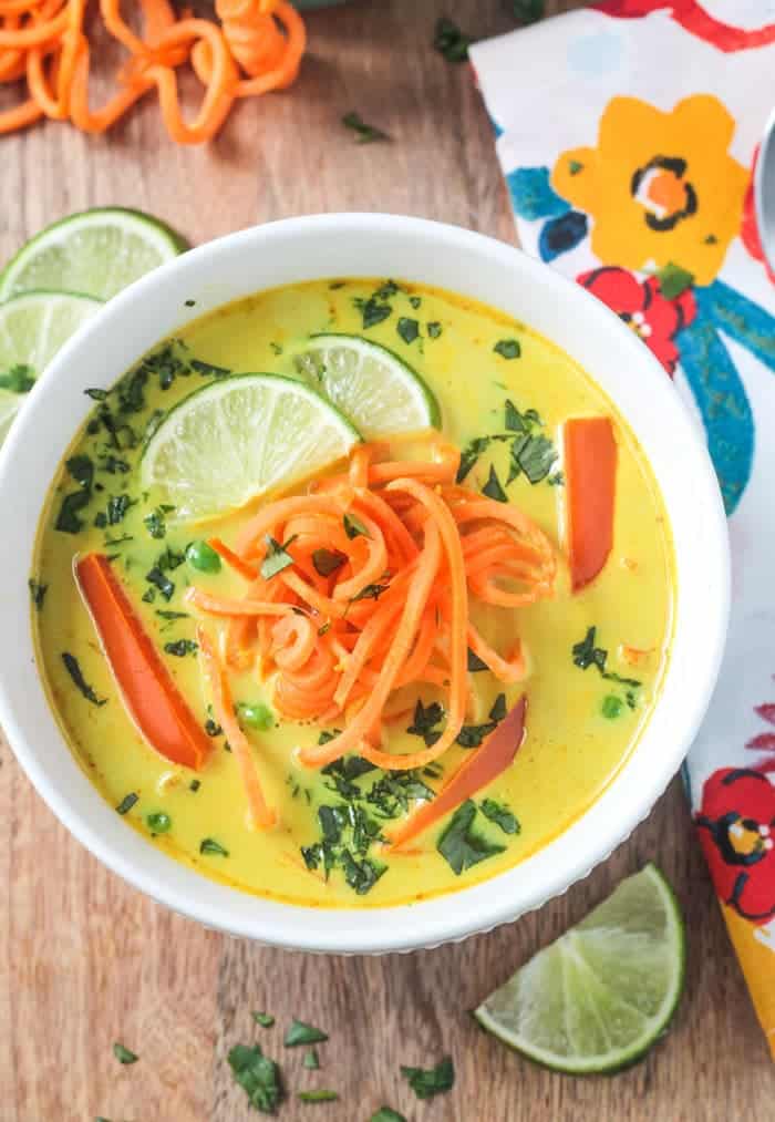 White bowl of coconut curry soup with sweet potato noodles on top and lime slices.