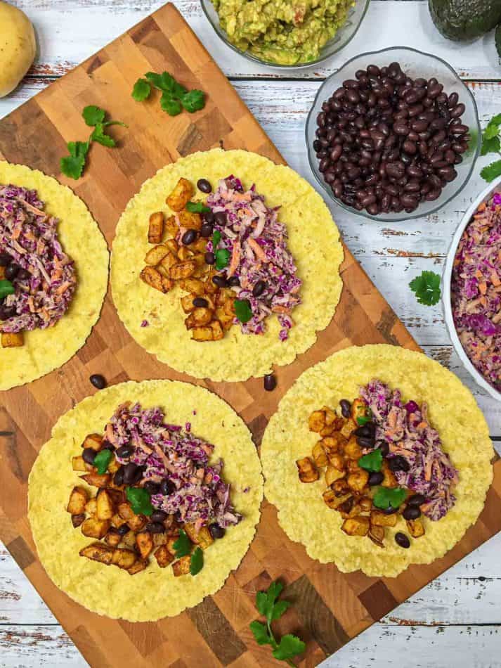 four tortilla wraps open on cutting board with potatoes and coleslaw on top