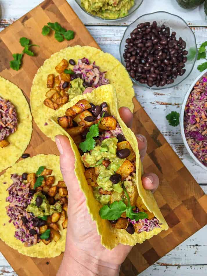 hand holding potato taco with black beans and guacamole