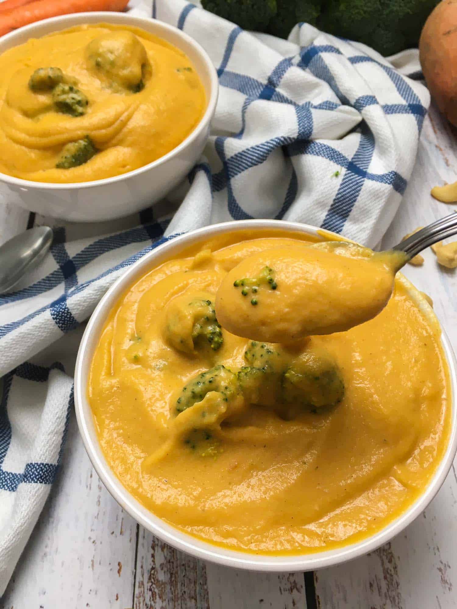 spoon of broccoli cheddar soup being held over bowl