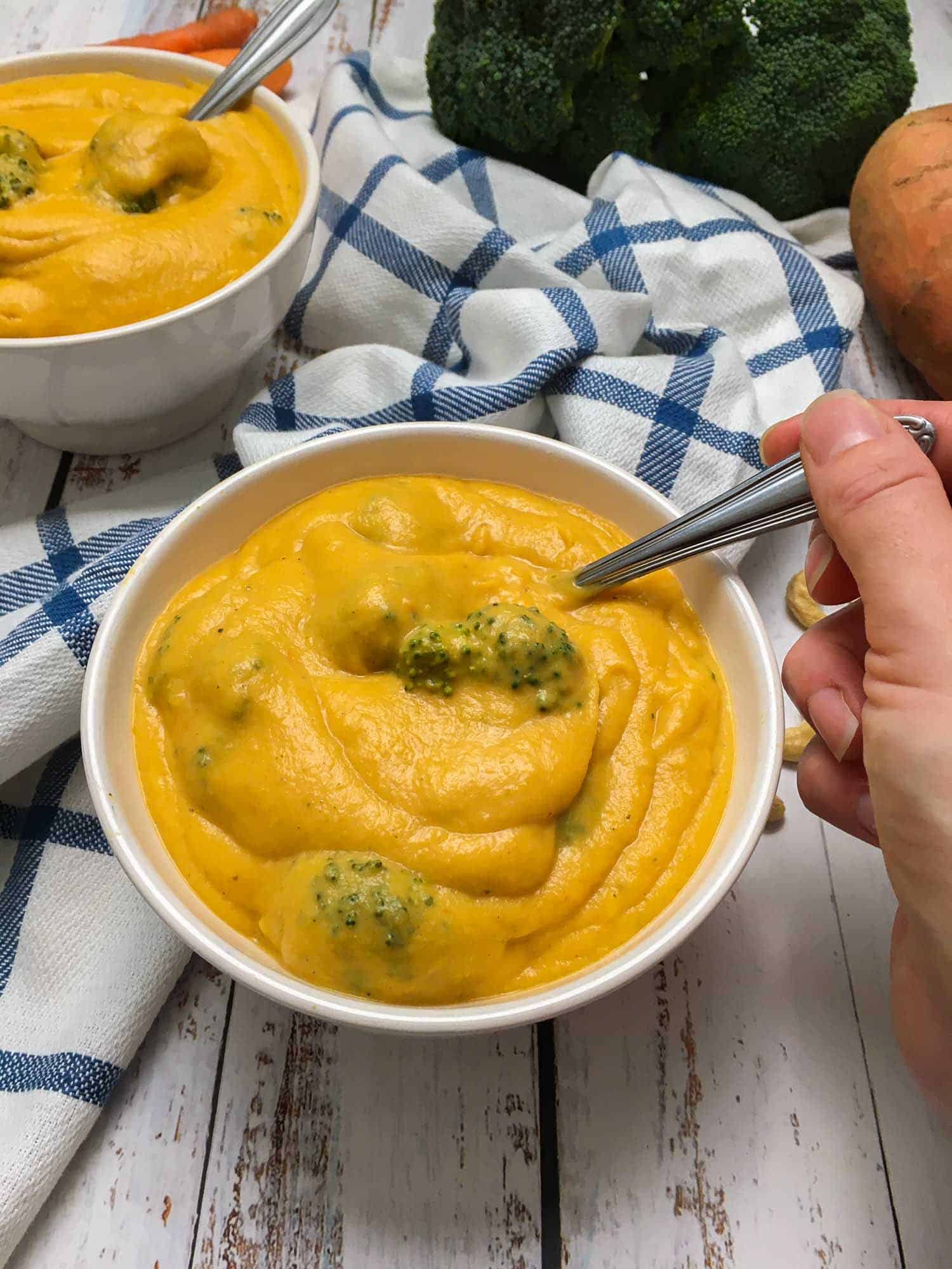 hand holding spoon inside bowl of broccoli cheddar soup