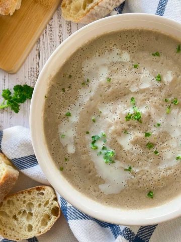 Bowl of creamy mushroom soup with baguette slices around the bowl.