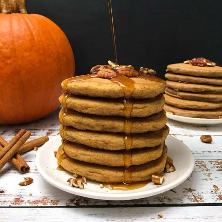 stack of pumpkin spice pancakes in plate with pumpkin in background.