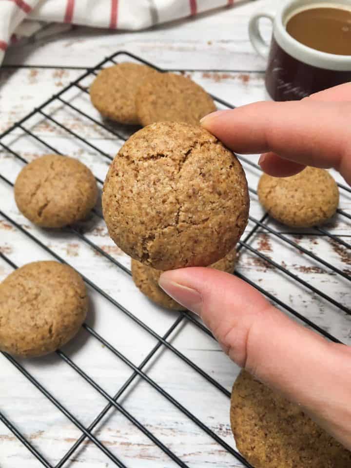 hand holding up cookie with more cookies on cooling rack in background