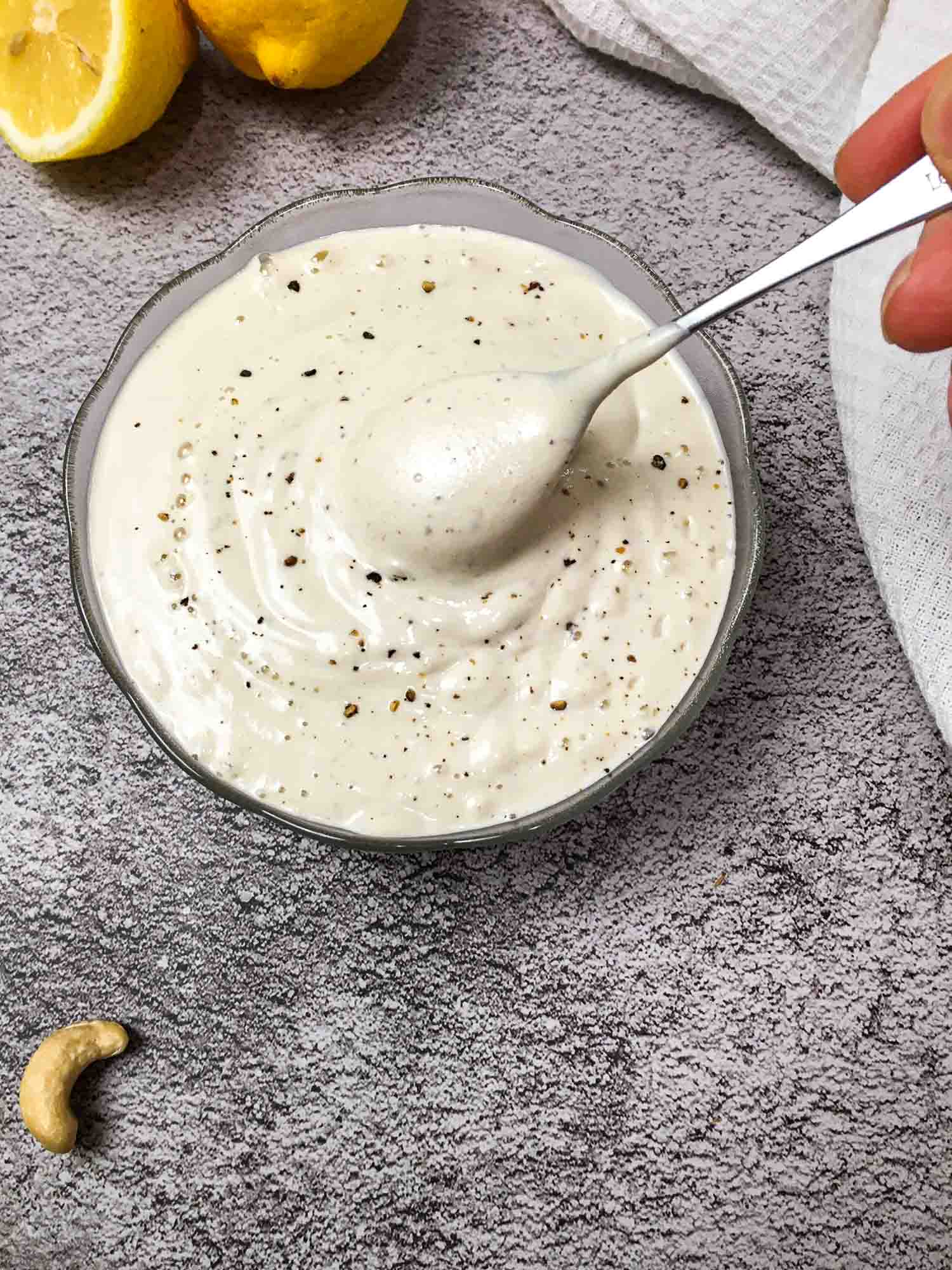 spoonful of vegan alfredo sauce being scooped out of glass bowl