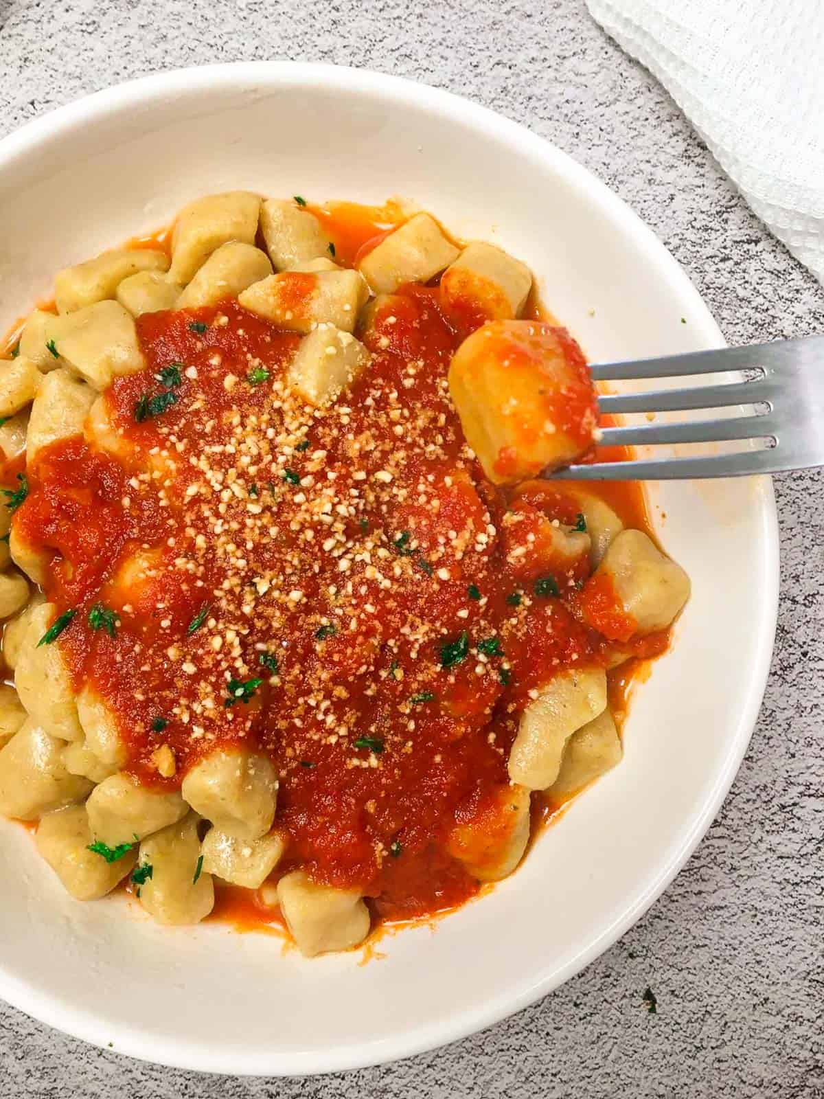 Fork holding up gnocchi with bowl below it.
