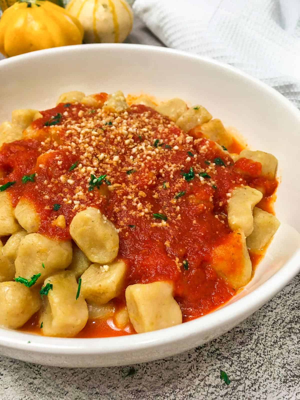 pumpkin gnocchi in white bowl with tomato sauce on top.
