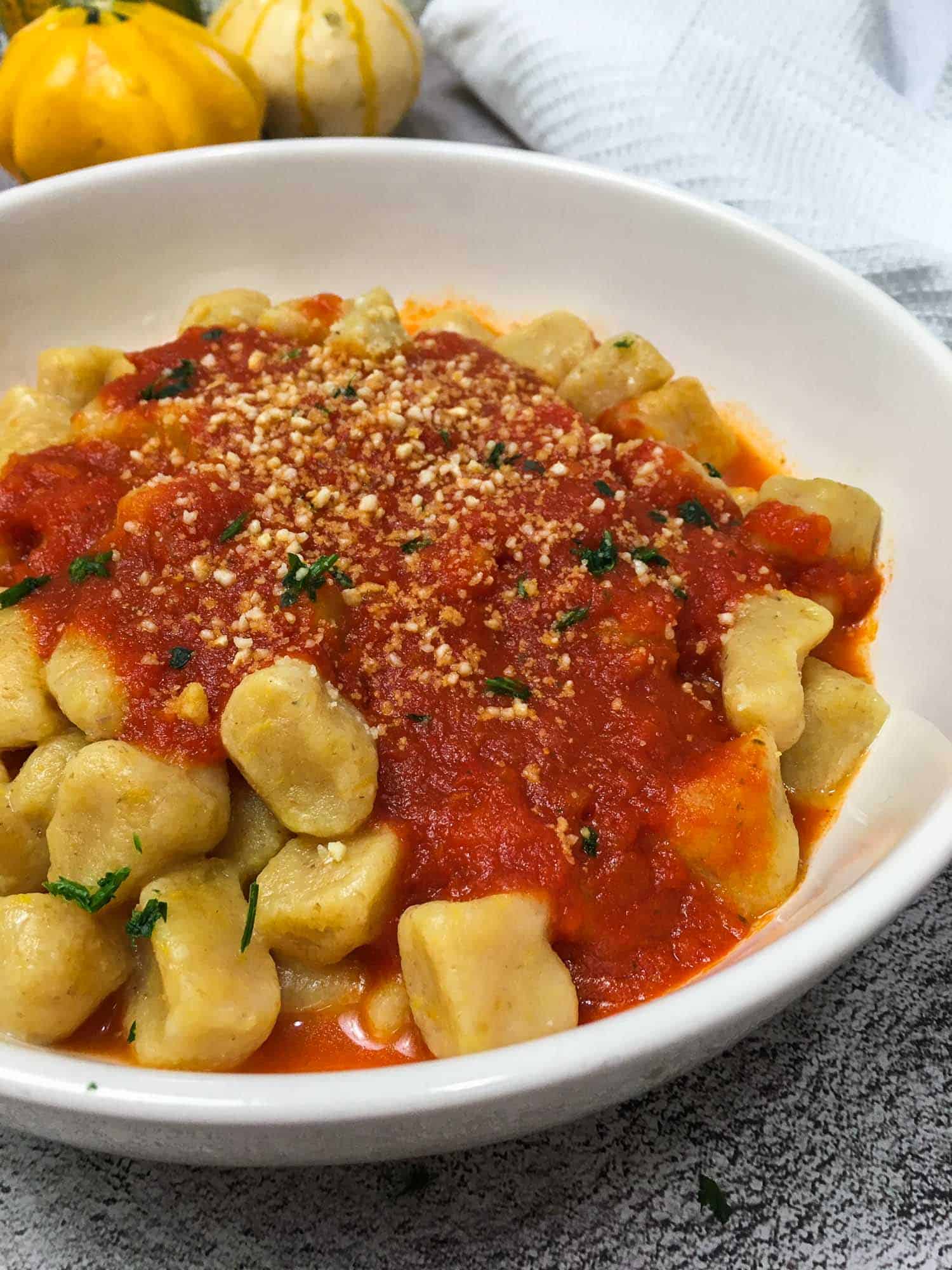 Pumpkin gnocchi in bowl with tomato sauce and parsley on top.
