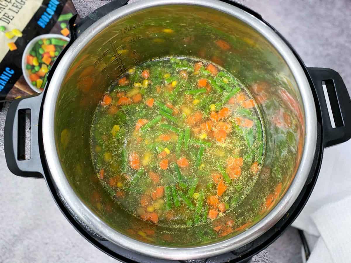 instant pot with veggies, rice, and broth inside, ready to cook
