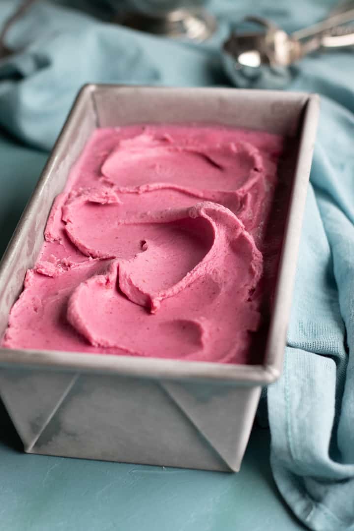 Cranberry ice cream in ice cream container with scoop in background.