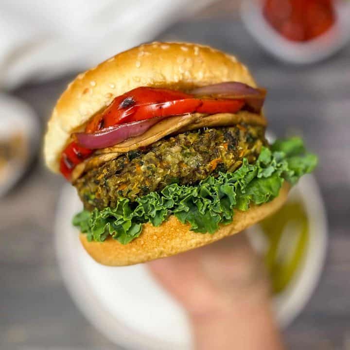 hand holding up veggie burger with lettuce, onion, and peppers inside