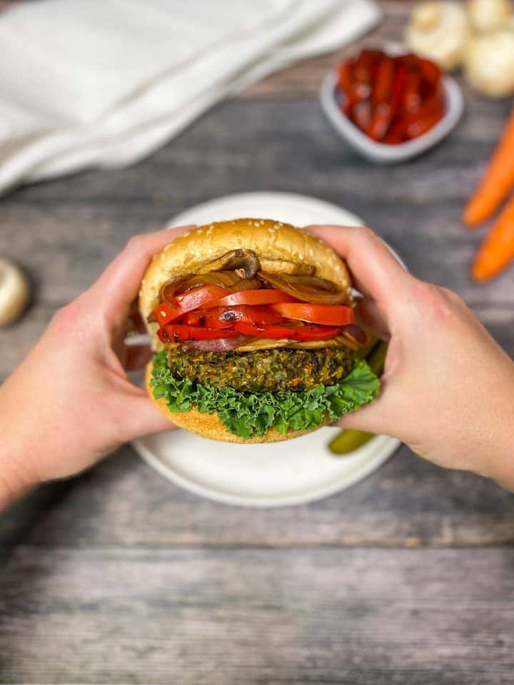 hands holding up mushroom risotto burger in bun with toppings