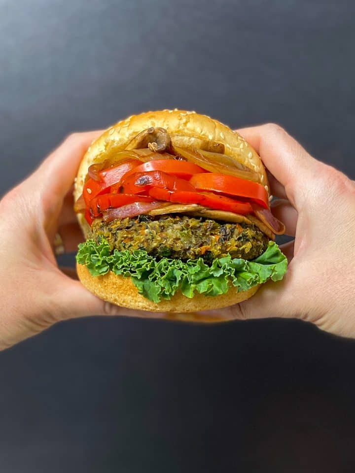 hands holding vegan mushroom risotto burger with lettuce, peppers, onions inside