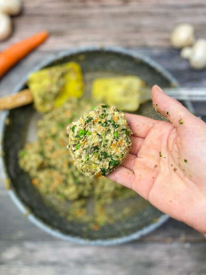 hand holding up vegetable mixture with skillet of batter below