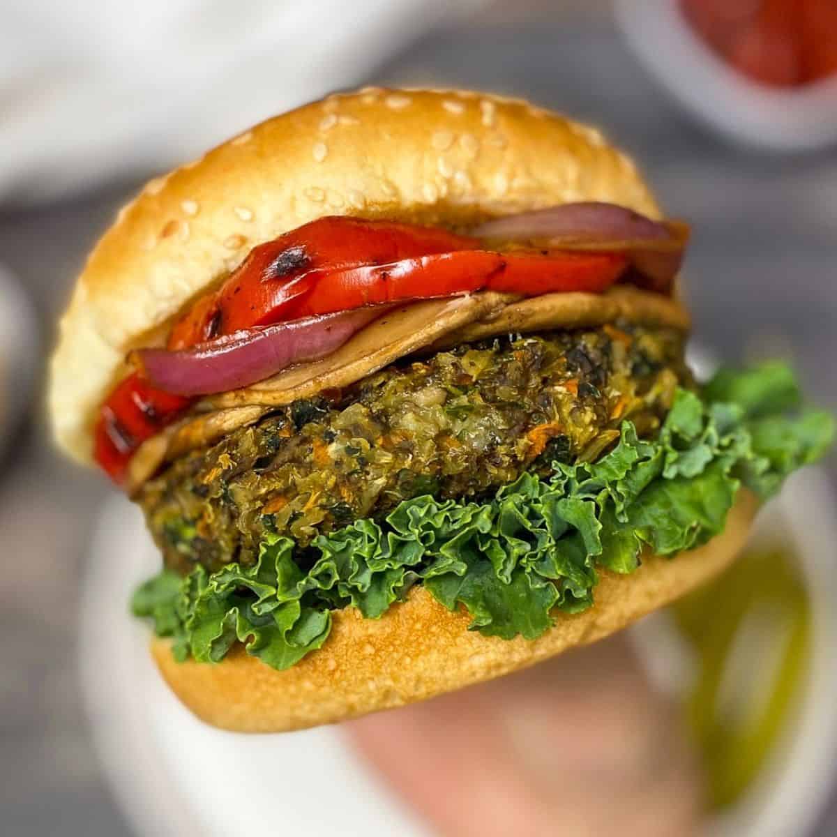 hand holding up veggie burger with lettuce, onion, and peppers inside
