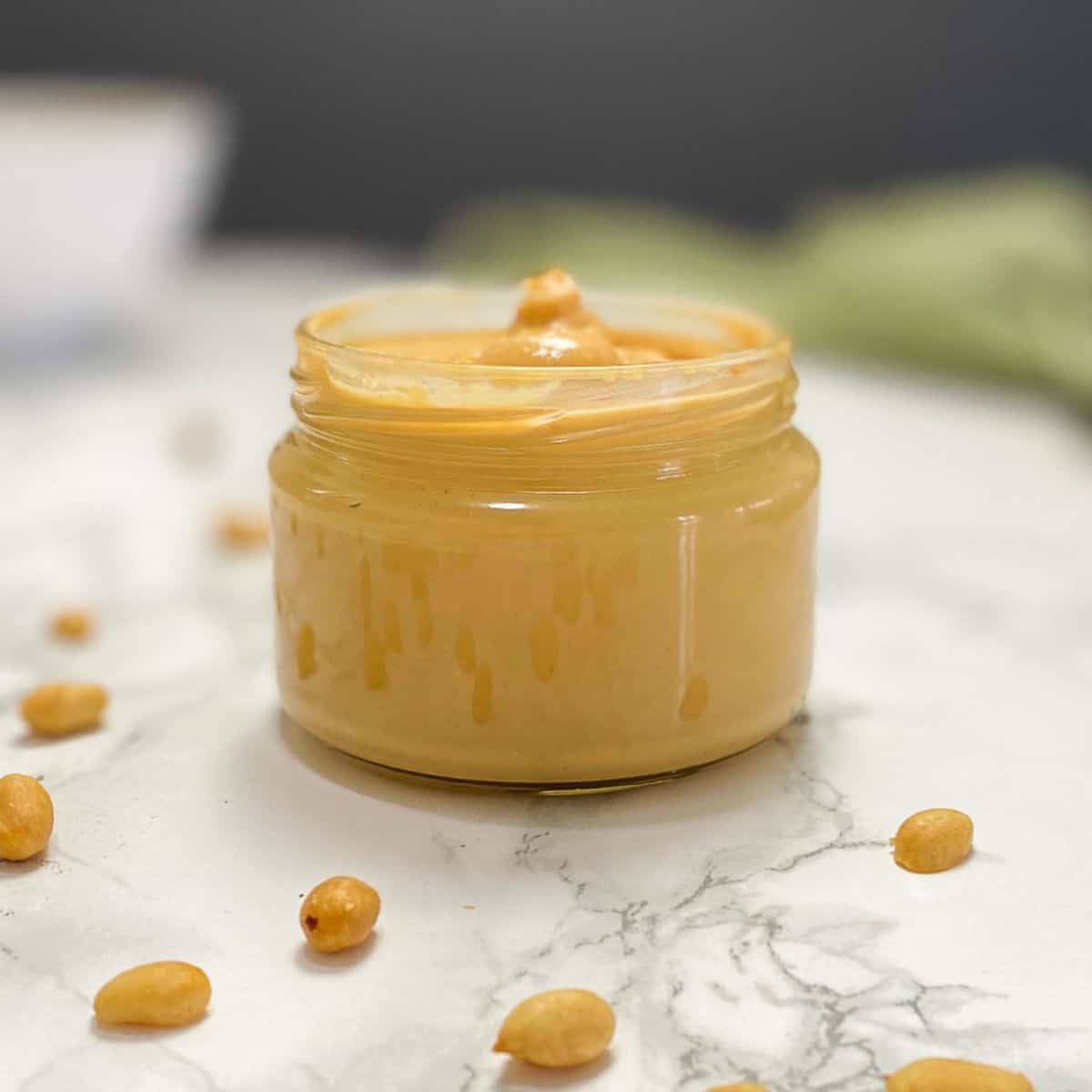 peanut butter in glass jar with peanuts scattered around the jar