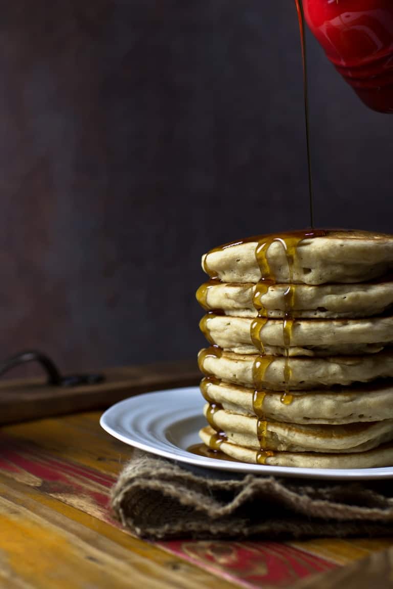 stack of vegan pancakes on white plate with maple syrup dripping down the sides