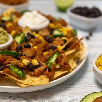 Platter of nachos with jackfruit, jalapeno, and corn on top.