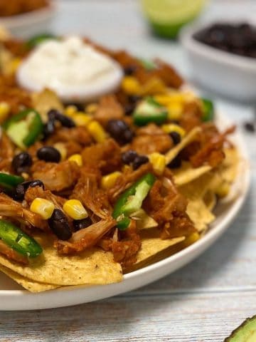 Platter of nachos with jackfruit, jalapeno, and corn on top.