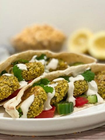 two open pitas on white plate with falafel and tahini