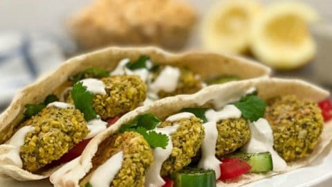 two open pitas on white plate with falafel and tahini