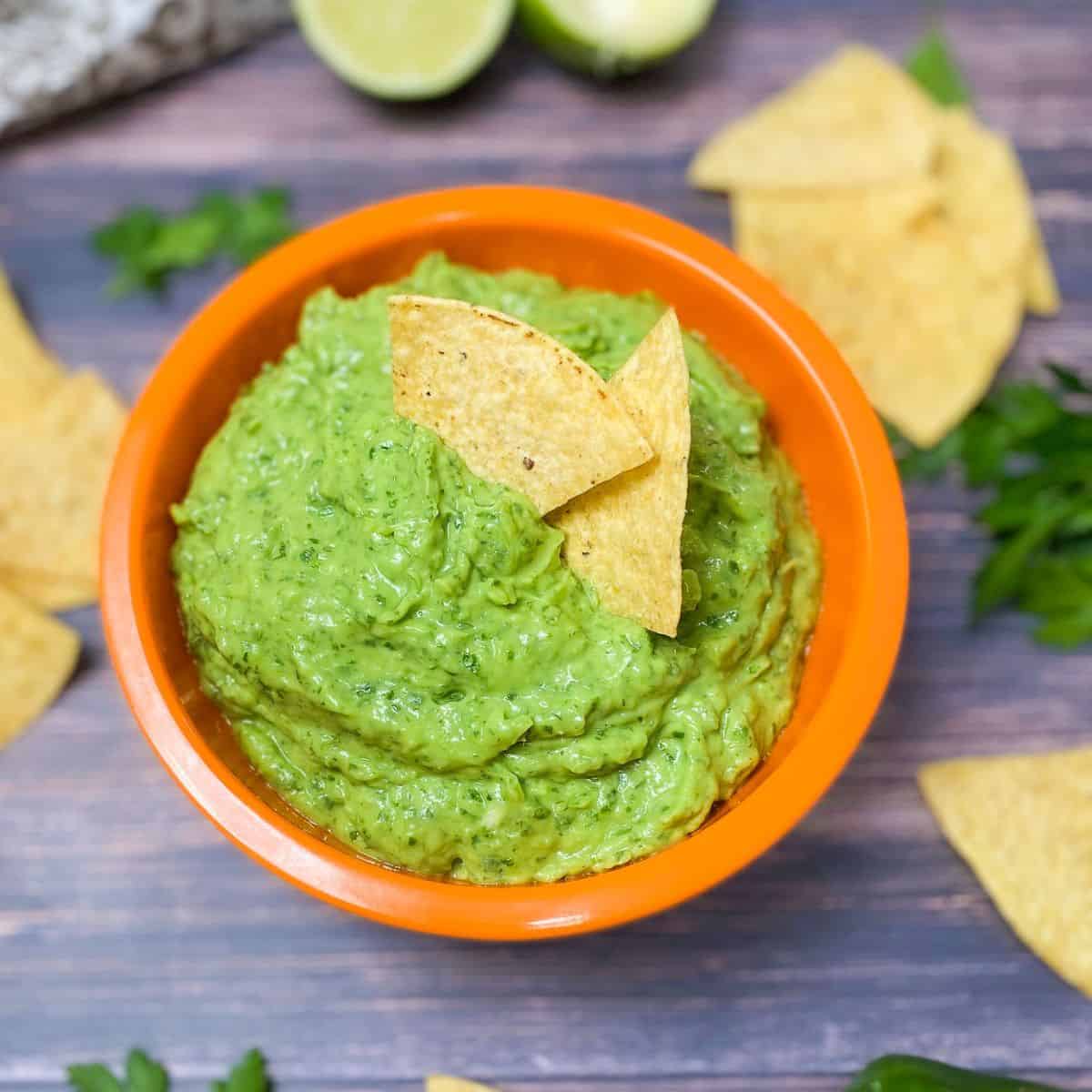 two tortilla chips resting in the center of a bowl of guasacaca dip