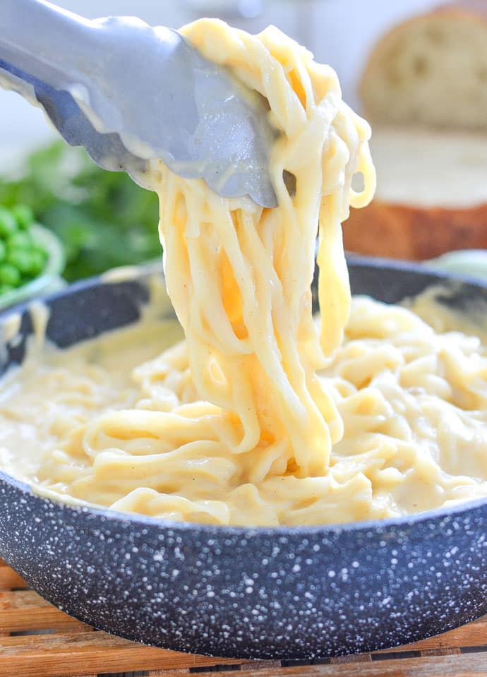 Tongs lifting fettuccine alfredo out of bowl