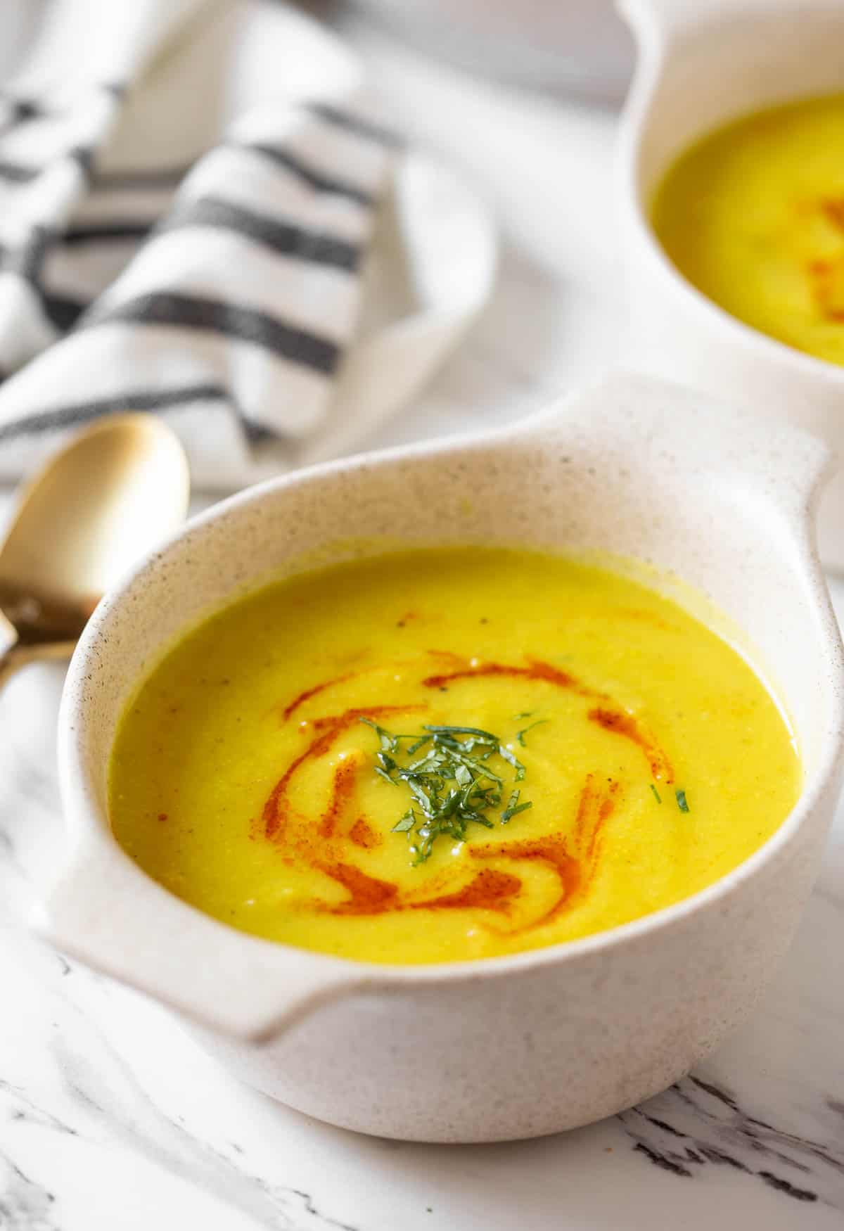 Bowl of yellow turmeric soup with green herbs garnished on top.