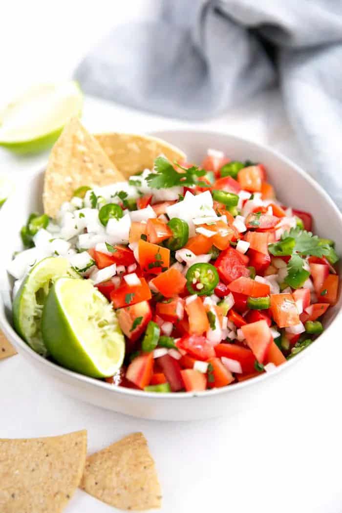 White bowl of chopped tomato, jalapeno and onion with lime garnish.