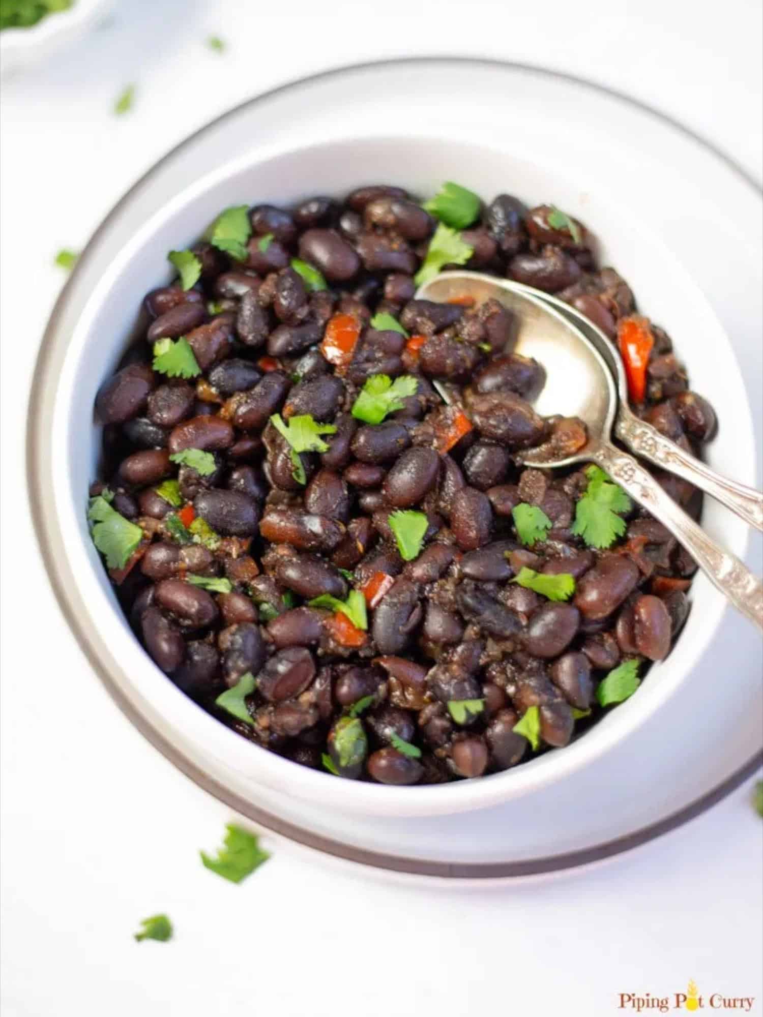 black beans in white bowl with spoon inside and cilantro garnish.