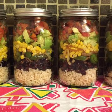 mason jar layered with rice, beans, corn, avocado and tomato.