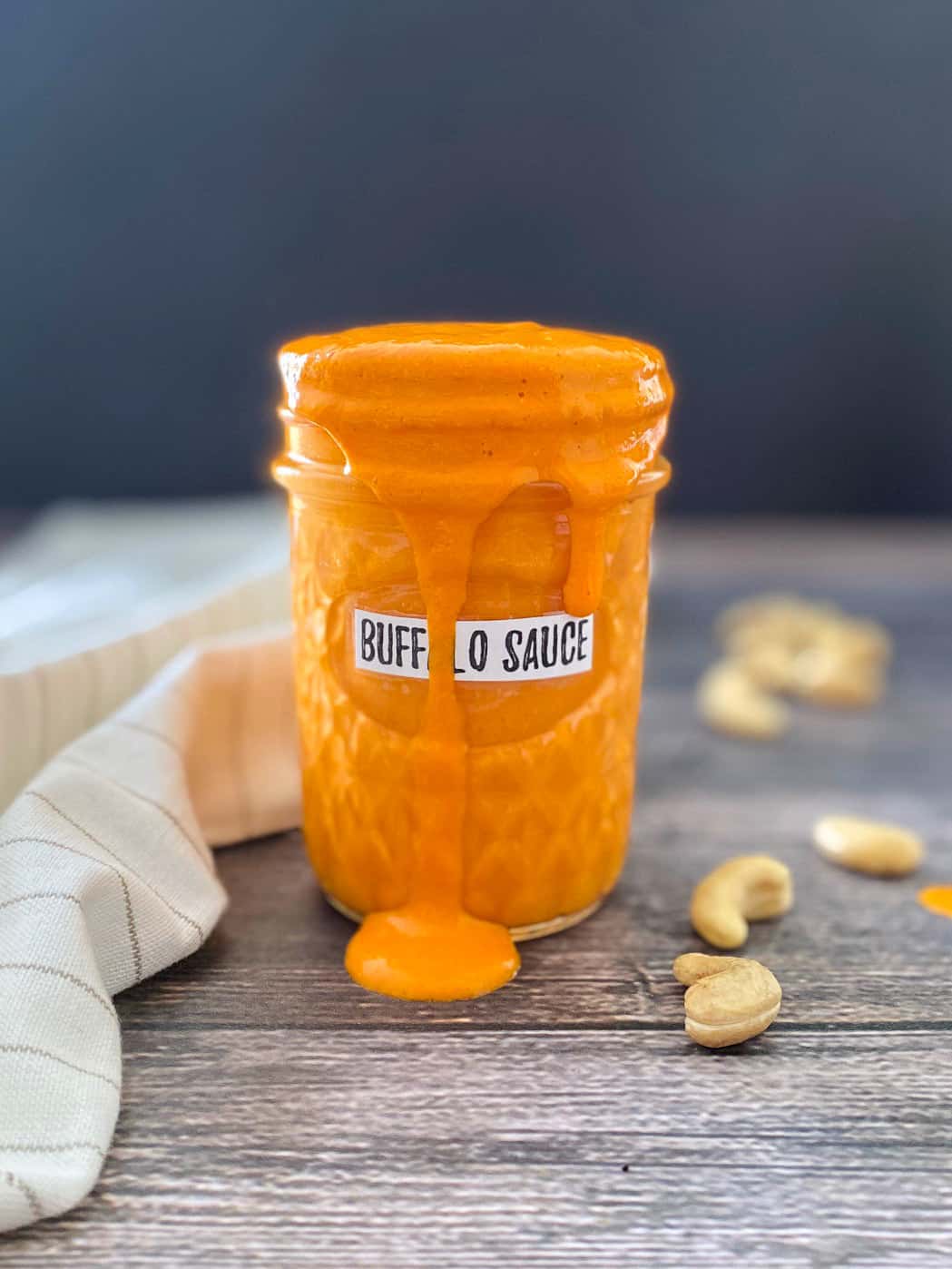 glass jar filled with vegan buffalo sauce that is spilling over the edges of the jar