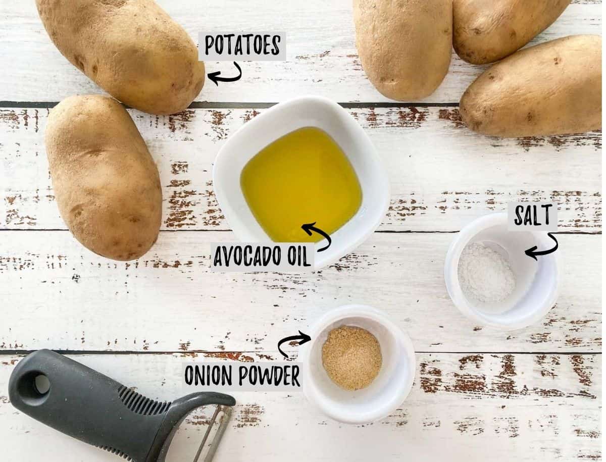 potatoes, oil, onion powder and salt on white deck with potato peeler beside them