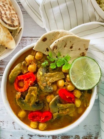 white bowl of chickpea mushroom curry with naan bread and lime garnish