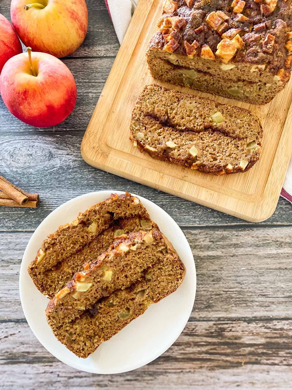 apple bread on cutting board and plate in front of the loaf with two slices on it.