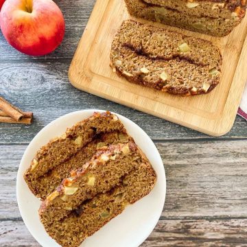 apple bread on cutting board and plate in front of the loaf with two slices on it.