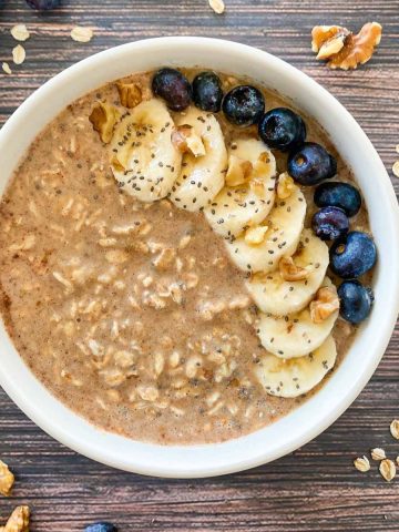 Bowl of oatmeal with banana slices, walnuts, blueberries and chia seed garnish.