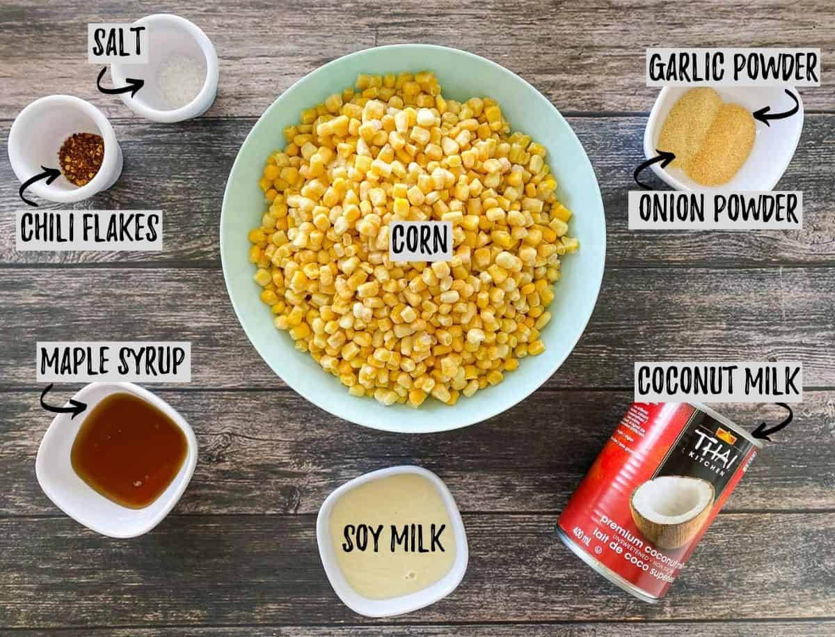 Ingredients needed to make vegan creamed corn scattered on dark grey deck.