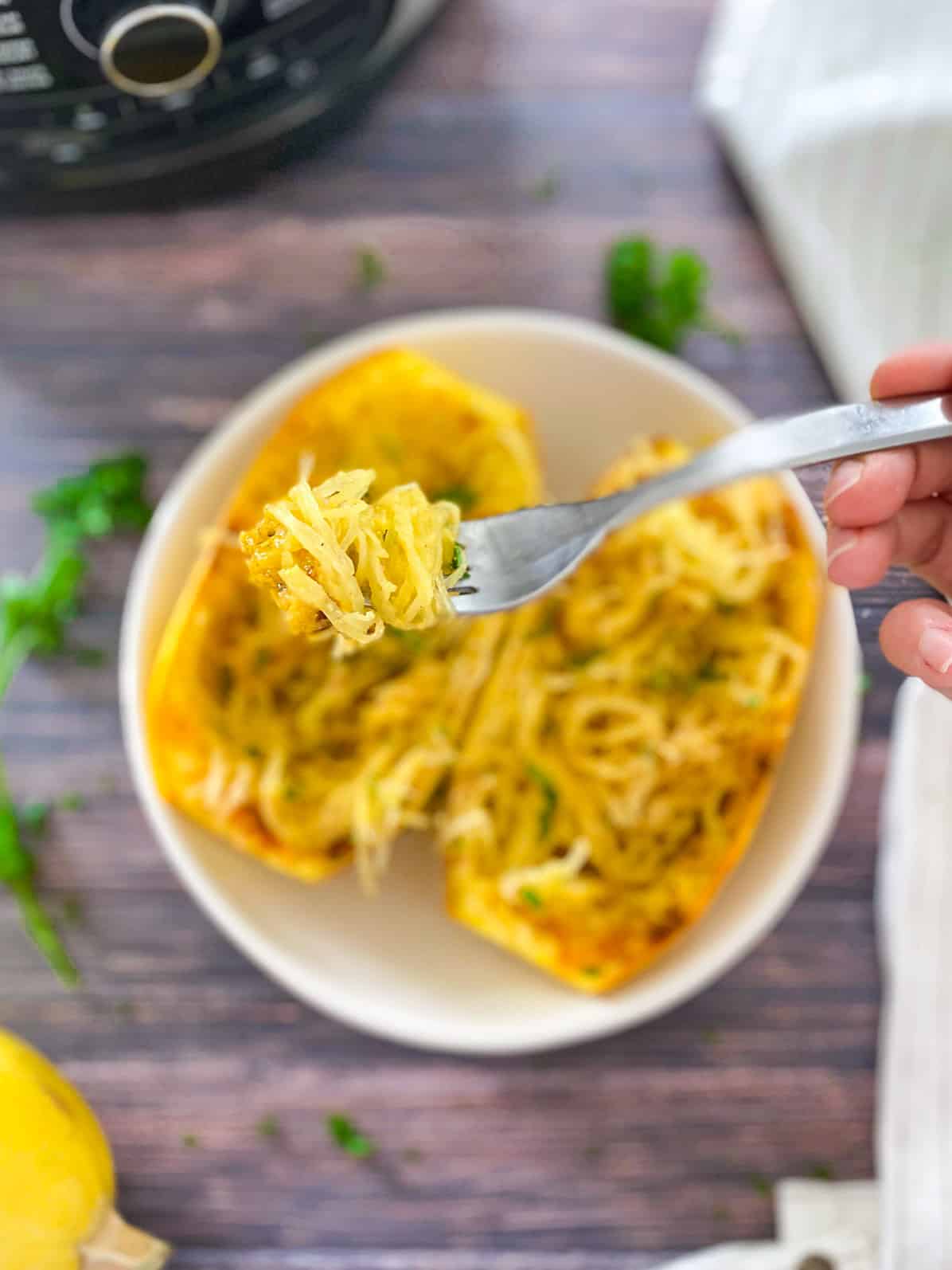 Fork full of spaghetti squash with halved spaghetti squash in bowl below and air fryer in the background.