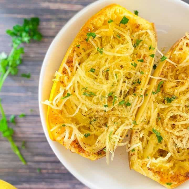 close up of cooked spaghetti squash sliced in half with parmesan cheese and parsley garnish on top.