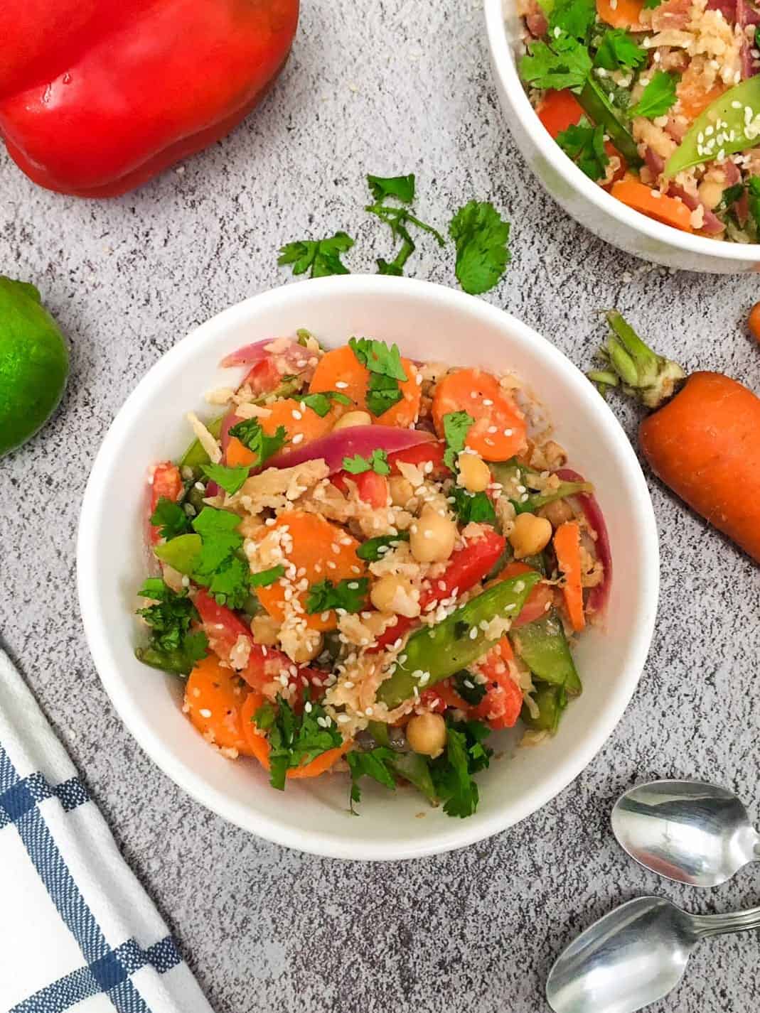 White bowl of stir fry with carrot, red pepper and lime surrounding the bowl.